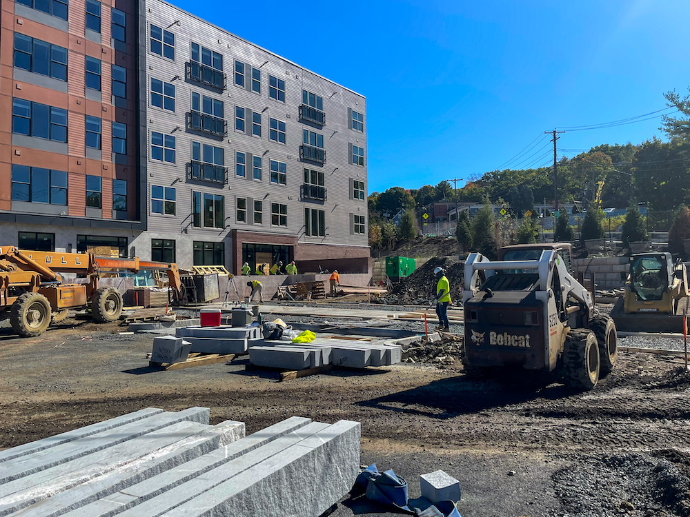 Active construction site with granite curbing installation and heavy equipment at Hanover Stoneham apartment development
