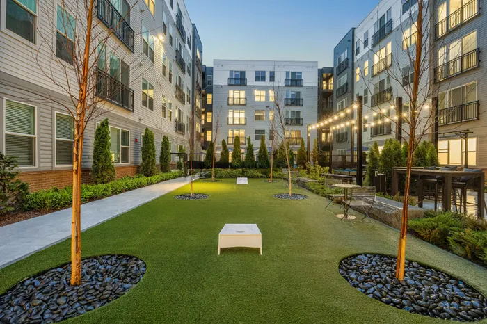 Apartment courtyard with turf lawn, seating area, and string lights at Hanover Stoneham residential community