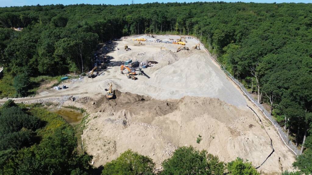 Drone view of the Franklin Grove Apartments construction site showing building pads, site roads, and surrounding wooded land