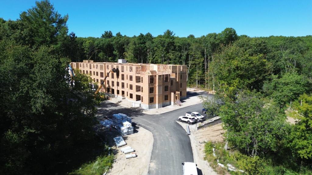 Drone view of multifamily building construction surrounded by wooded areas at Franklin Grove Apartments in Franklin, MA.